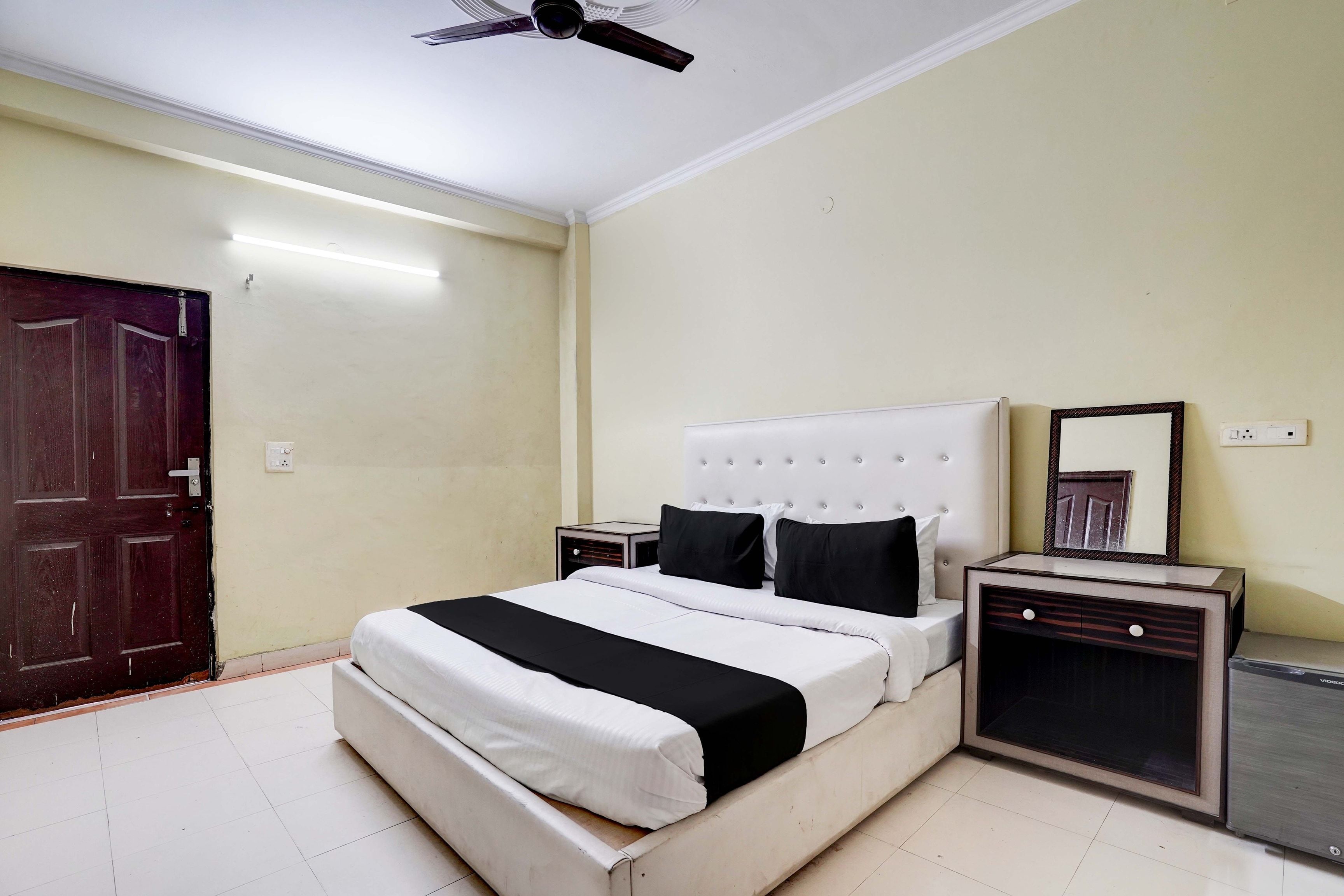 Una habitación de hotel con cama, mesita de noche, espejo y ventilador de techo.