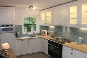 A kitchen with white cabinets, a gas stove, a dishwasher, and a window with a view of greenery. - hollandferien.haus Strandperle 83 (Julianadorp aan zee)