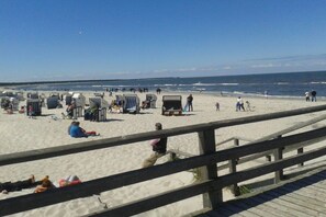 A beach with rows of beach chairs and umbrellas, a wooden boardwalk, and the ocean in the background. - Holiday apartment with 1 bedroom (Fuhlendorf)