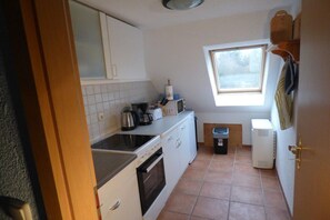 A compact kitchen with white cabinets, a stove, a microwave, and a window providing natural light. - Holiday apartment with 1 bedroom (Fuhlendorf)