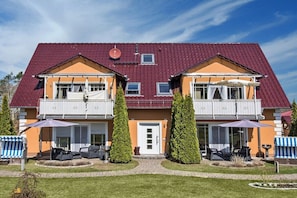 Ein zweistöckiges Haus mit rotem Dach und einem Balkon im oberen Geschoss sowie einer Haustür.