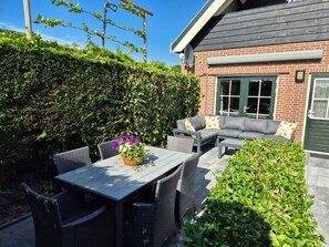 An outdoor patio area with a table and chairs, a sofa, and a hedge. - Bungalow Ellemeet (Ellemeet)