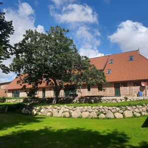 Ein traditionelles Backsteingebäude mit geneigtem Dach, Steinmauern und einem großen Baum im Vordergrund.