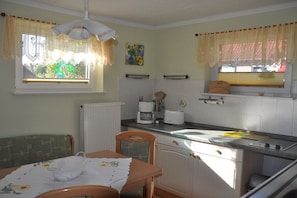 A compact kitchen with a dining area, a radiator, a coffee maker, and a window with curtains. - Holiday apartment with 2 bedrooms (Sassnitz)