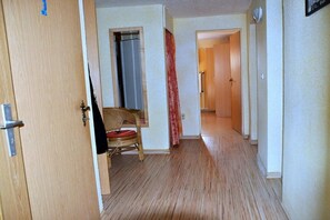 A hallway with a wooden floor, a wicker chair, and a door leading to another room. - Holiday apartment with 2 bedrooms (Sassnitz)