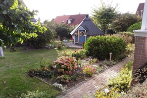 Un giardino con una piccola casa blu, un vialetto in mattoni e diverse piante.