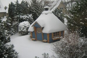 A snow-covered wooden cabin with a steep roof, surrounded by snow-laden trees and houses. - Holiday apartment with 2 bedrooms (Sassnitz)