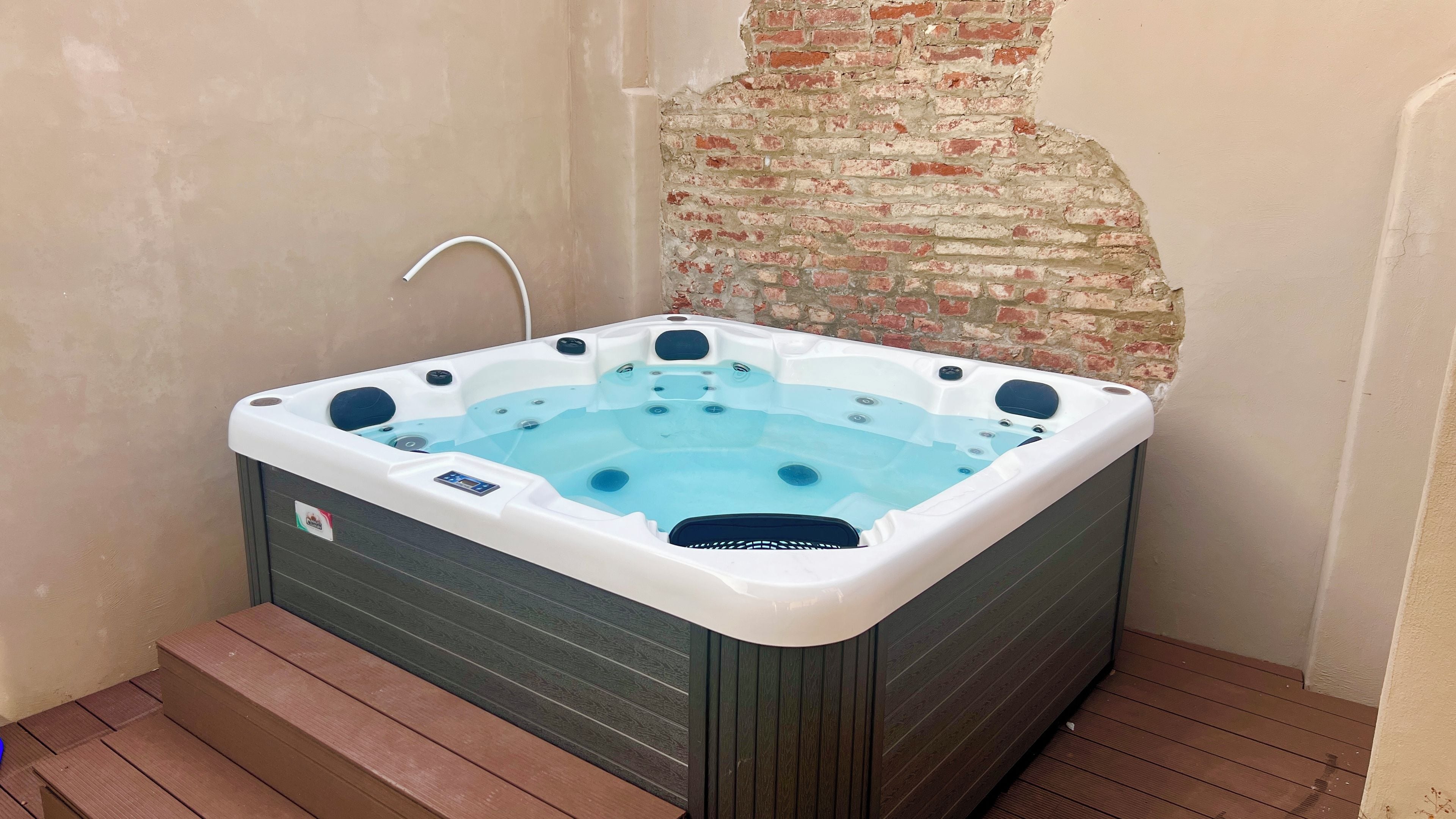 A hot tub with a control panel, surrounded by wooden steps and a brick wall.