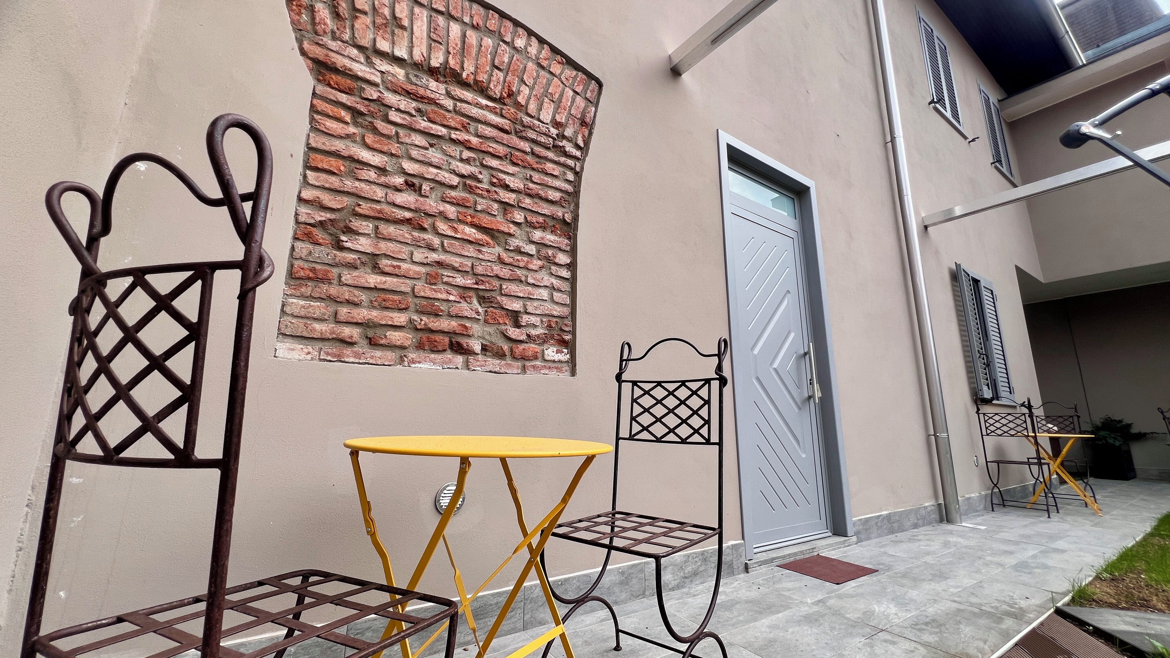 Fachada de edificio con pared de ladrillo, una puerta y mobiliario exterior.