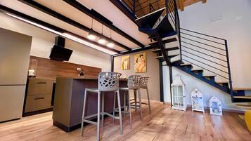 A modern kitchen with a wooden countertop, bar stools, and a staircase with a black railing.