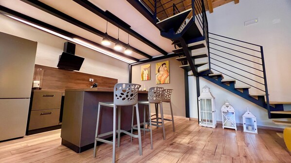 A modern kitchen with a wooden countertop, bar stools, and a staircase with a black railing.