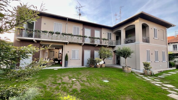 A two-story building with a balcony, a small garden, and a paved walkway.