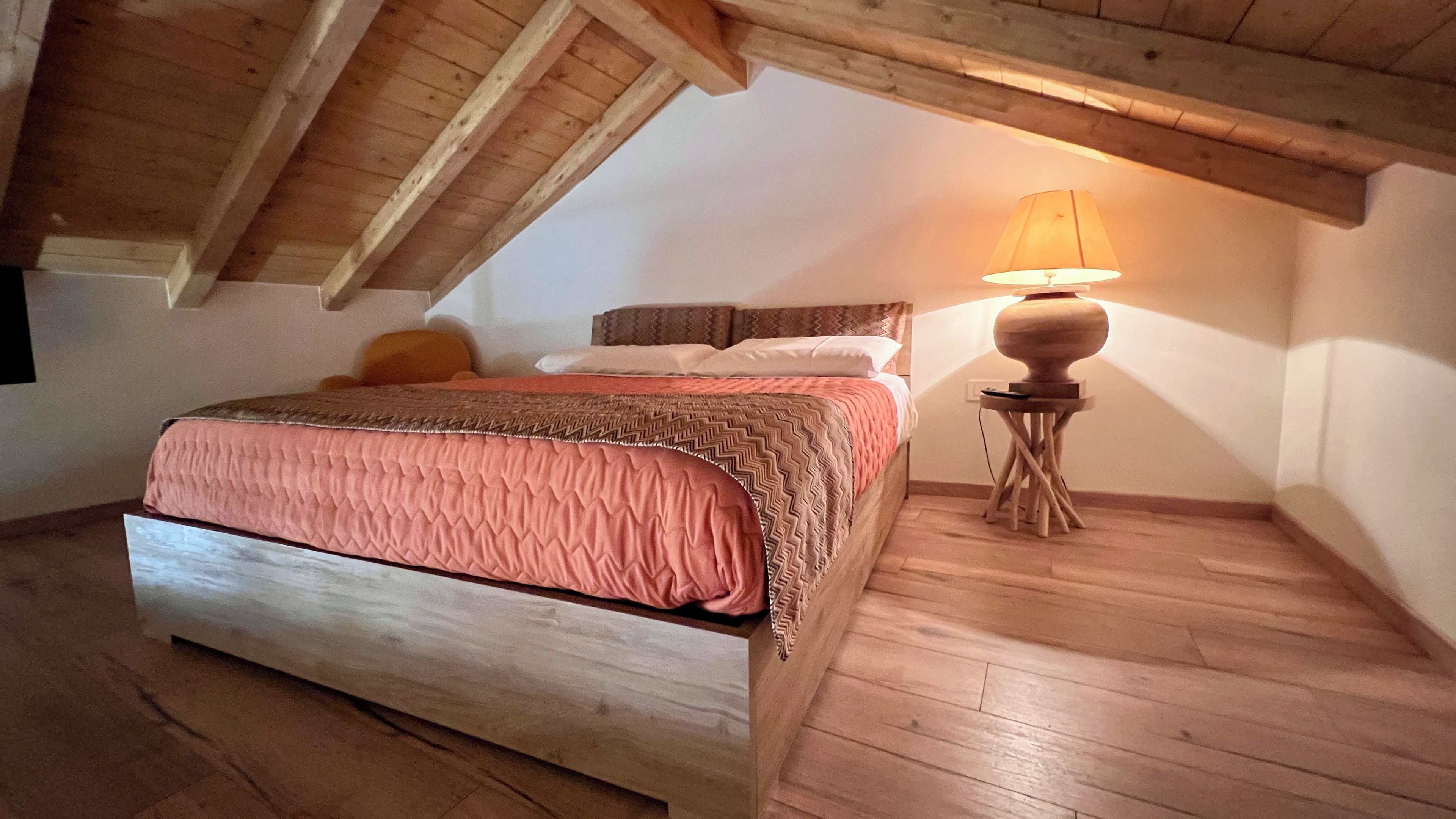 A bedroom with a wooden bed, a bedside lamp, and a sloped ceiling.