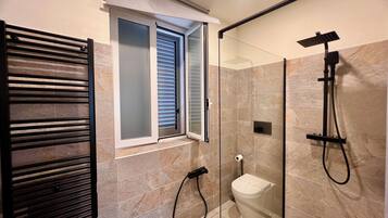 Un baño moderno con cabina de ducha de vidrio, un perchero y un inodoro.