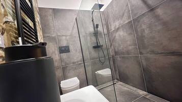 Un baño moderno con ducha, inodoro y un contenedor negro grande, posiblemente un cubo de basura.