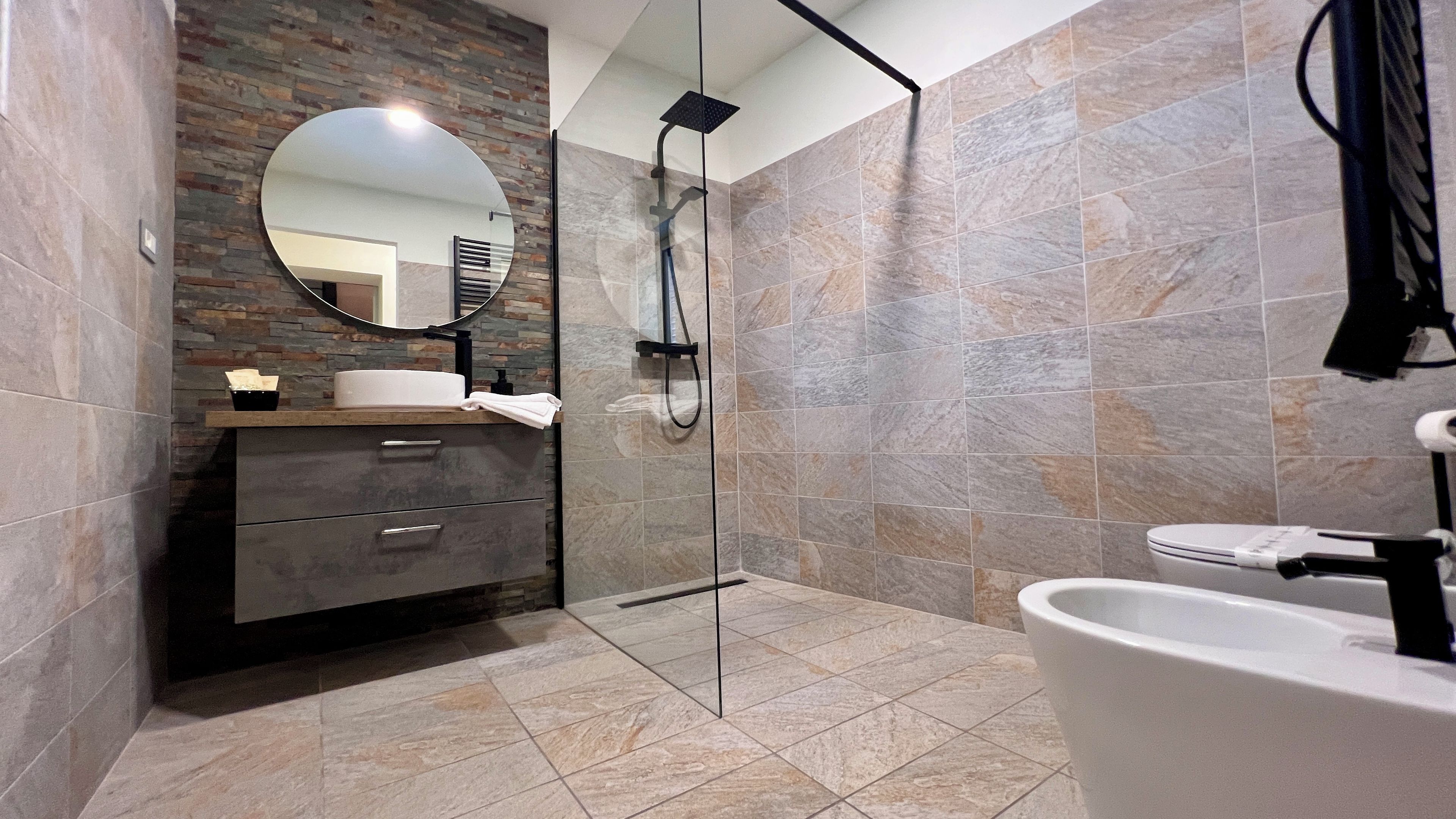 Un baño moderno con ducha envuelta en vidrio, un espejo redondo y un tocador con lavamanos.