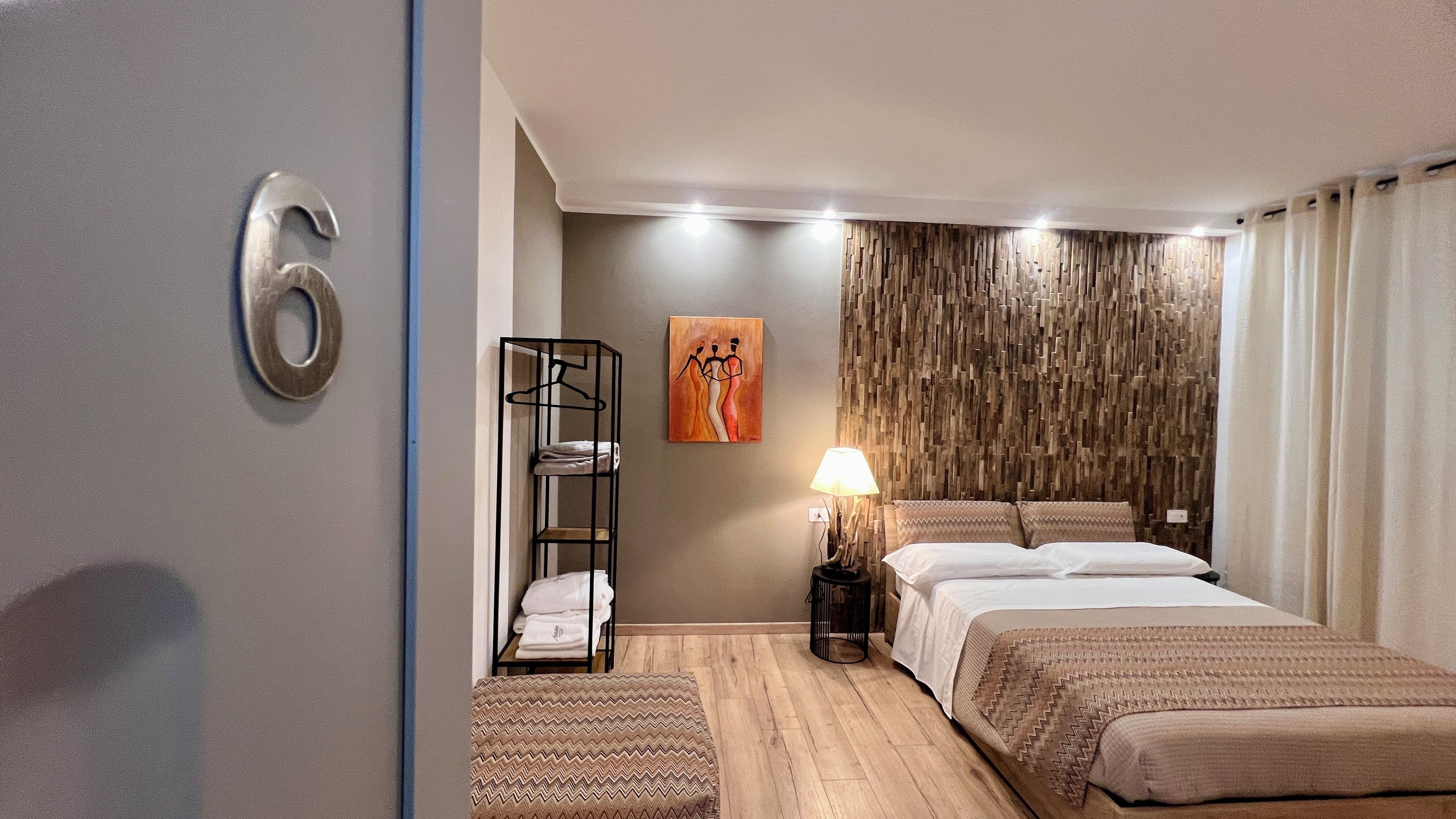A hotel room with a bed, a bedside table with a lamp, a wall-mounted artwork, and a wooden wall panel.
