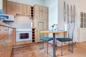 A compact kitchen with wooden cabinets, a built-in oven, and a small dining area with two chairs. - Villa Sabinium - Apartment 02 (Seebad Heringsdorf)