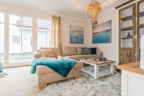 A living room with a sofa, a coffee table, and a chandelier. There are paintings on the wall and a view through the glass door. - Holiday home in Zingst with swimming pool (Zingst)