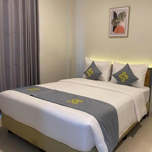 Habitación de hotel con cama, dos almohadas, una colcha y un cuadro en la pared.