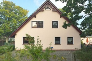 Kaksikerroksinen talo, jossa on harjakatto, useita ikkunoita ja aidattu piha.