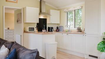 A compact kitchen with white cabinets, a microwave, a coffee maker, and a window with a view of greenery.