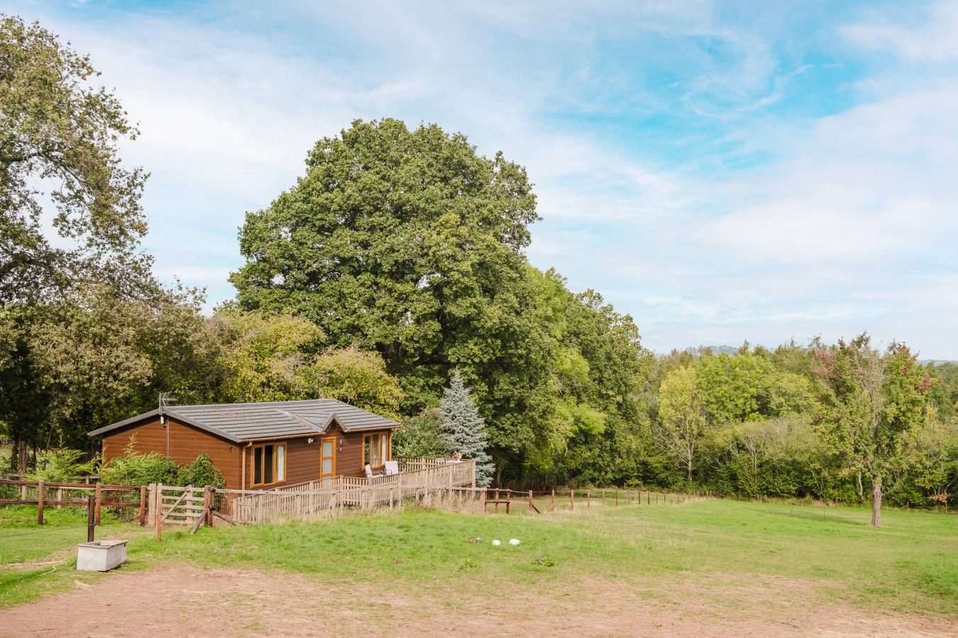 A wooden cabin with a fenced yard, surrounded by trees.