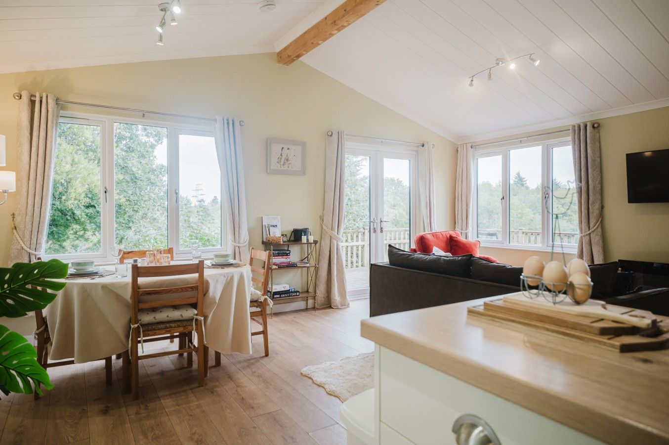 A well-lit room with a dining table, chairs, a sofa, and a kitchen area with a countertop.