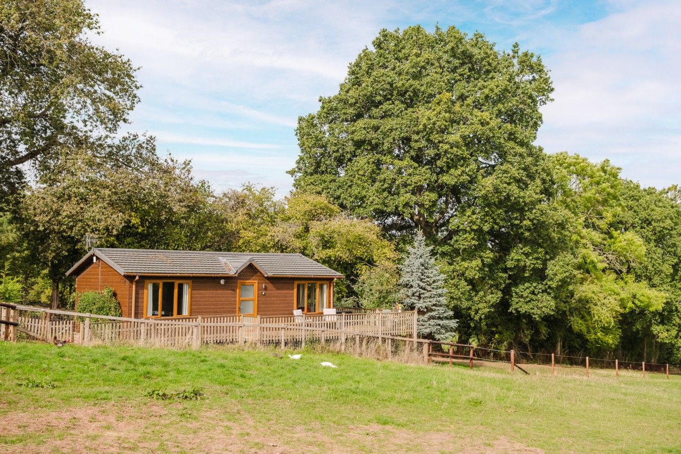 A wooden cabin with a fenced yard, surrounded by trees.