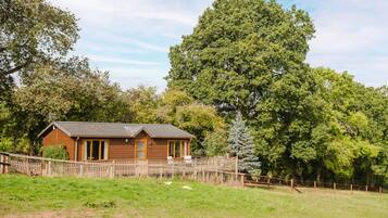 A wooden cabin with a fenced yard, surrounded by trees.