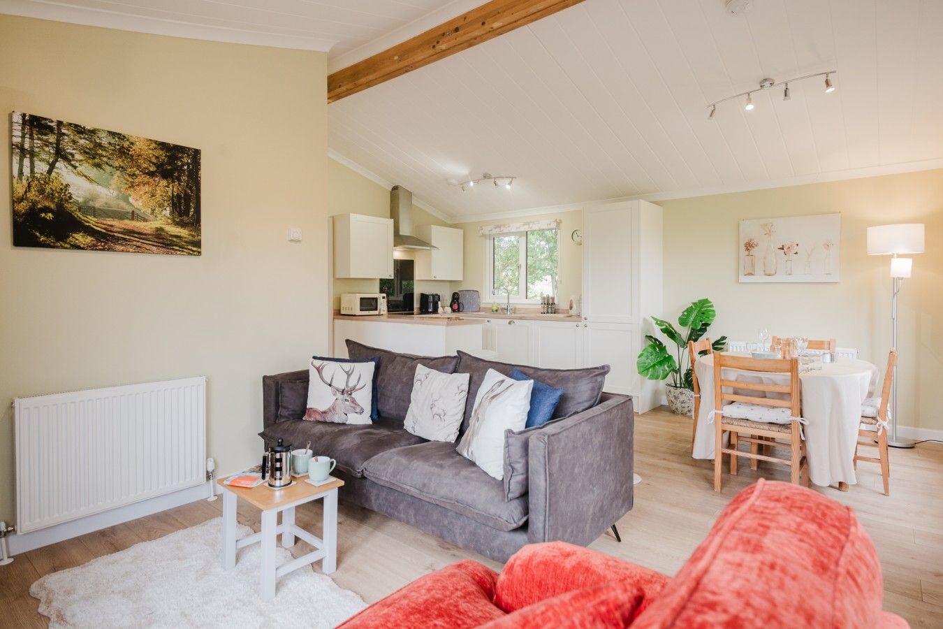 A cozy living room with a grey sofa, a red chair, a white radiator, and a dining area with a table and chairs.