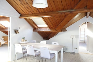 A room with a sloped ceiling, a dining table with chairs, a radiator, and a lamp. - Apartment in Oostkapelle with Wifi (Oostkapelle)