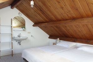 A bedroom with a sloped ceiling, a built-in sink, a bedside table, and a bed with white bedding. - Apartment in Oostkapelle with Wifi (Oostkapelle)