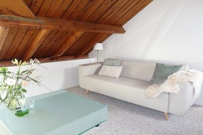 Een moderne woonkamer met een glazen salontafel, een witte bank met kussens en een houten plafond.