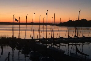 Een jachthaven in de zonsondergang, met meerdere boten aan de kade en vlaggen op palen.