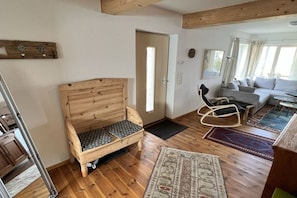 Een houten bed met hoofdeinde, een grijze bank en een vloerkleed met patroon in een kamer met houten vloer en een deur die naar een andere kamer leidt.