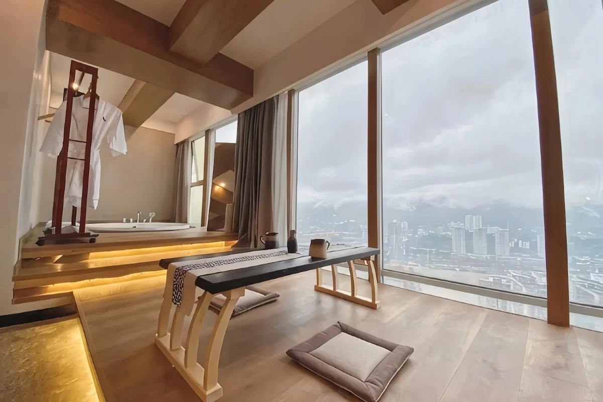 A modern room with a large window, a wooden desk, a bench, and a clothing rack.