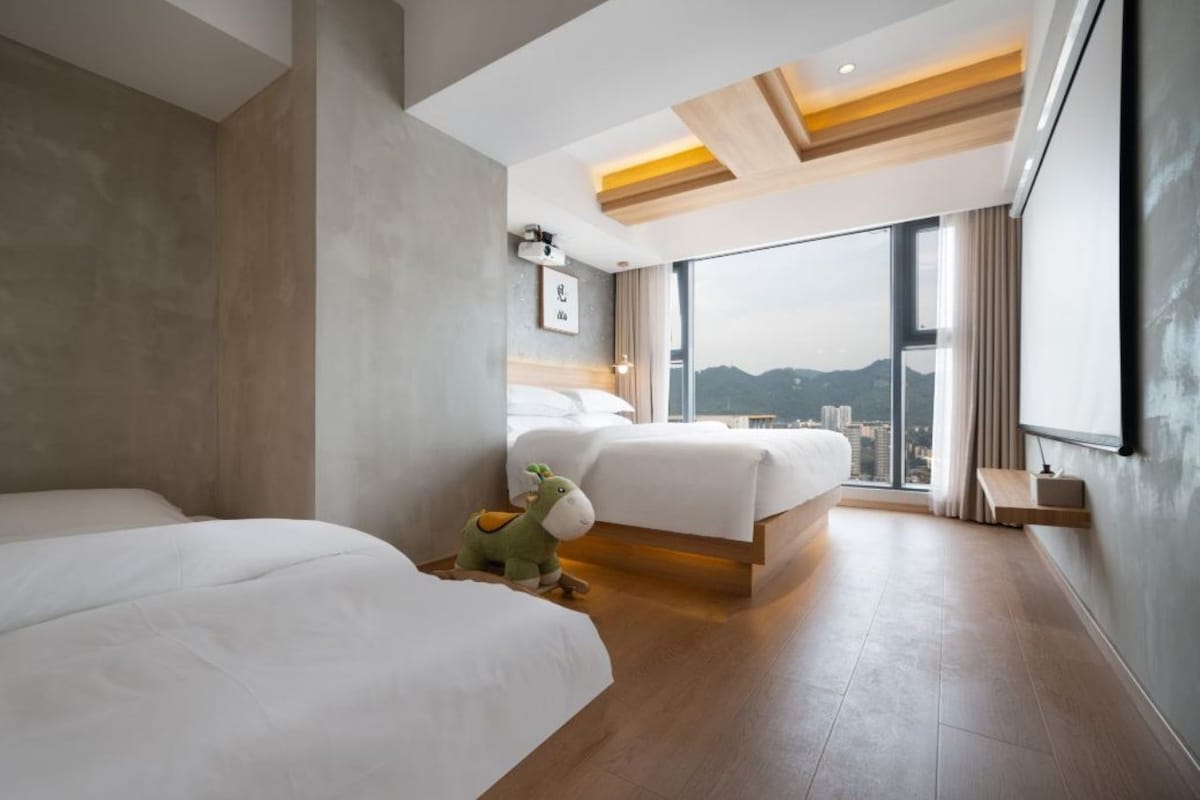 A modern hotel room with two beds, a city view, and a wooden ceiling.