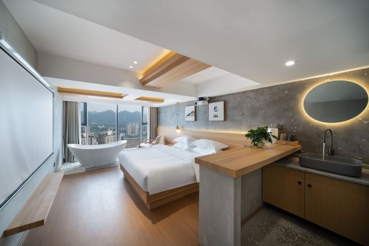 A modern hotel room with a large bed, a bathtub, and a city view.