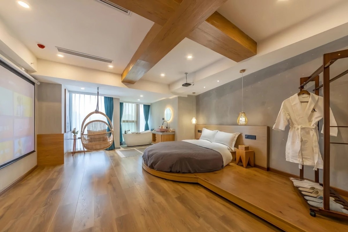 A modern bedroom with a curved bed, a wooden floor, a hanging chair, and a robe rack.