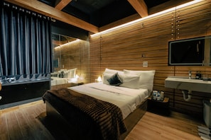 A modern hotel room with a large bed, a bedside table with a lamp, a bathroom with a sink and mirror, and wooden paneling on the walls. - Atlantis Tran Duy Hung Apartment (Yen Hoa)