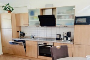 Cozinha moderna com armários de madeira, forno embutido, máquina de café e micro-ondas.