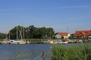 Ruhige Wasserfläche mit angestaubten Booten, umgeben von Grünflächen und Gebäuden mit roten Dächern.