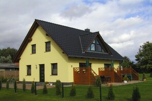 Ein zweistöckiges Haus mit einem geneigten Dach, einer Holztreppe und einem umzäunten Garten.