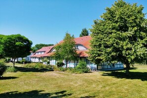 A traditional house with a red roof, surrounded by a well-maintained lawn and trees. - Holiday apartment with 1 bedroom (Dranske)