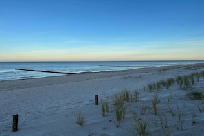 A beach with a wooden jetty extending into the water, sandy dunes, and sparse vegetation. - Holiday home with 1 bedroom (Fuhlendorf)