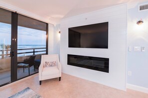 Ett modernt vardagsrum med en stor TV som är monterad på väggen, en bekväm fåtölj och utsikt över havet genom en skjutdörr i glas.