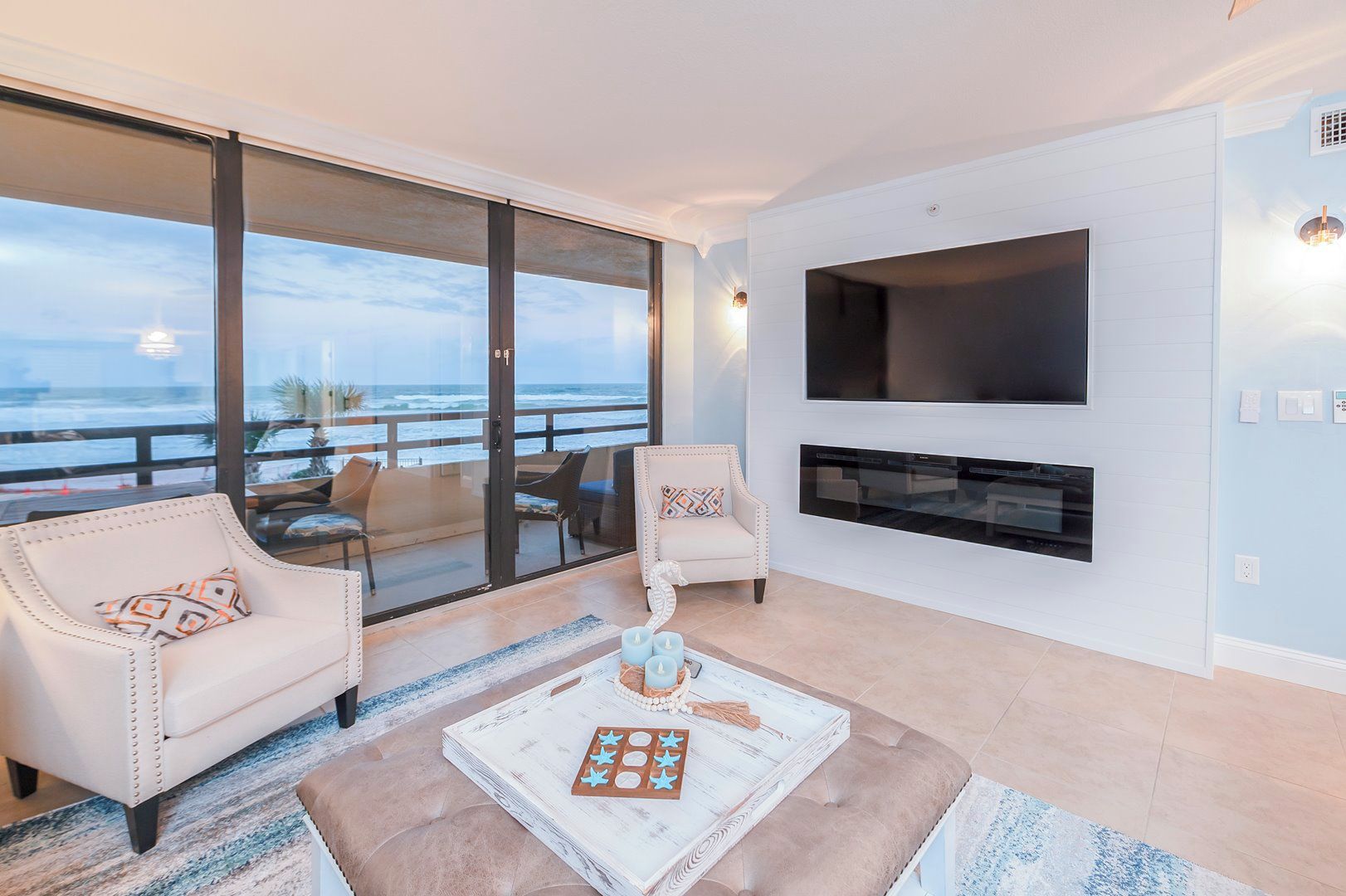 A modern living room with a large TV, comfortable seating, and a view of the ocean.