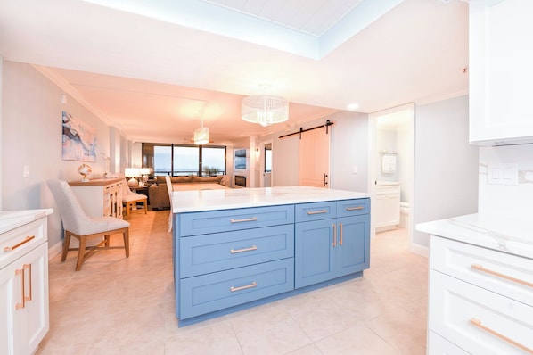 Cozinha moderna com ilha central, armários azuis e vista para a sala de estar.