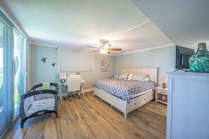 A bedroom with a bed, a desk, a chair, a crib, a ceiling fan, and a television. - 1030 EastWinds S in Ponce Inlet, FL (Ponce Inlet)